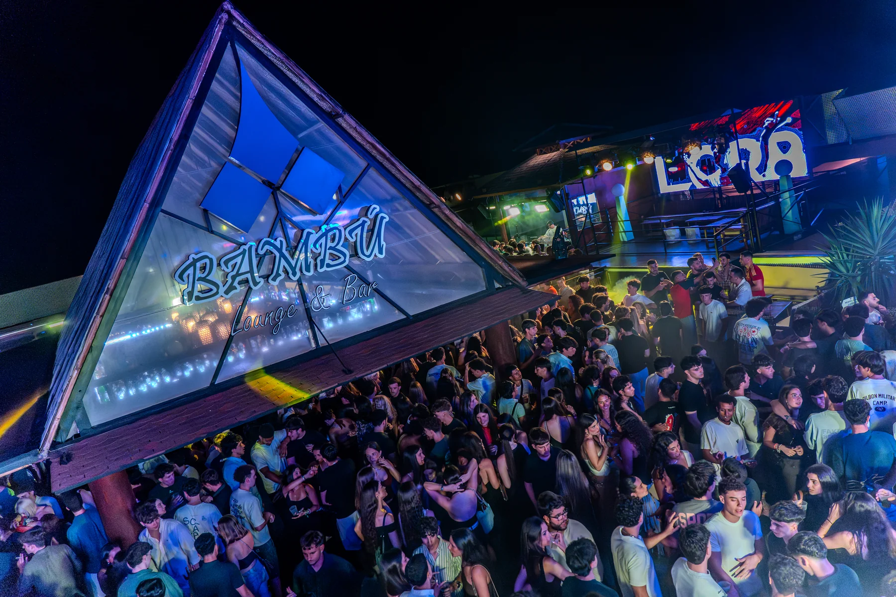El exterior del local lleno de gente bajo la pirámide iluminada